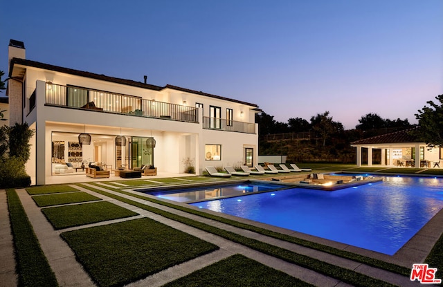 pool at dusk with an in ground hot tub, an outdoor structure, and a patio area