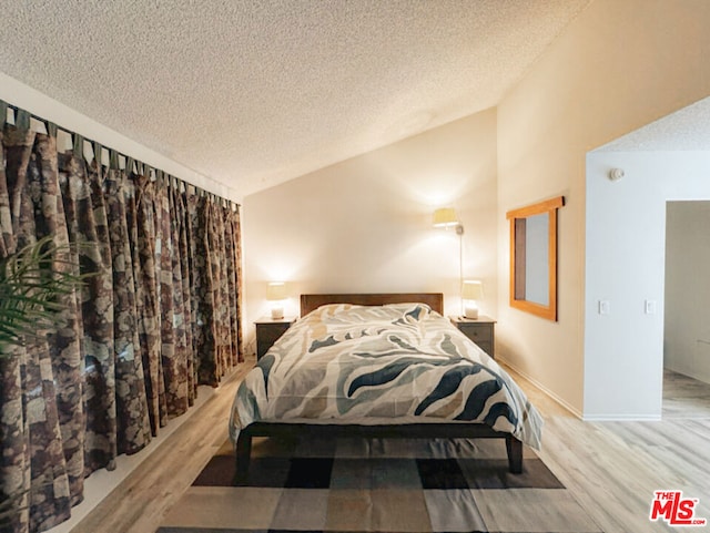 bedroom with hardwood / wood-style flooring, vaulted ceiling, and a textured ceiling