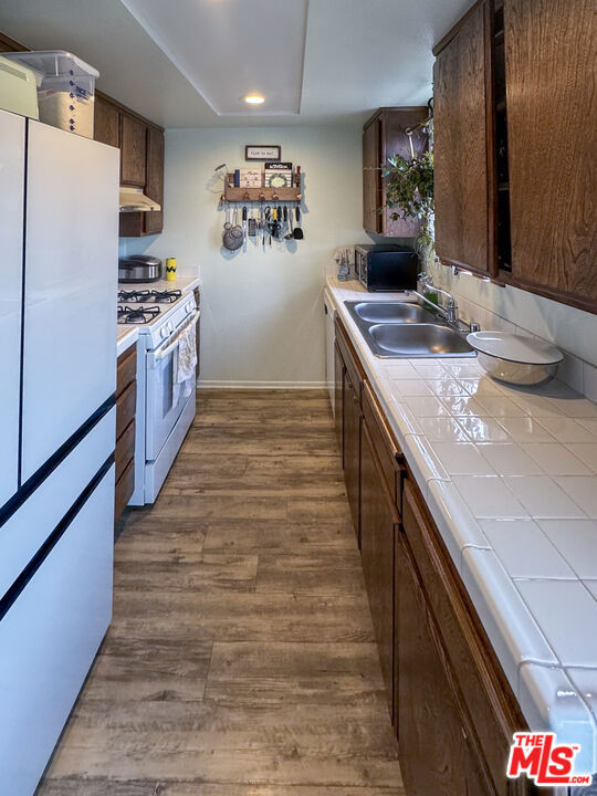 kitchen featuring sink, white appliances, dark brown cabinets, dark hardwood / wood-style floors, and tile countertops