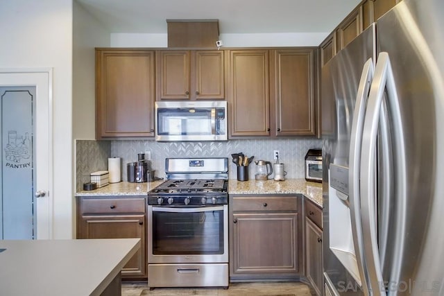 kitchen with decorative backsplash, light stone countertops, and appliances with stainless steel finishes