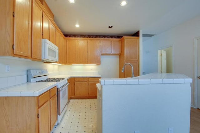 kitchen featuring white appliances, sink, tile counters, and an island with sink