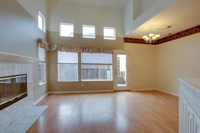 unfurnished living room featuring a towering ceiling, a fireplace, a chandelier, and light wood-type flooring