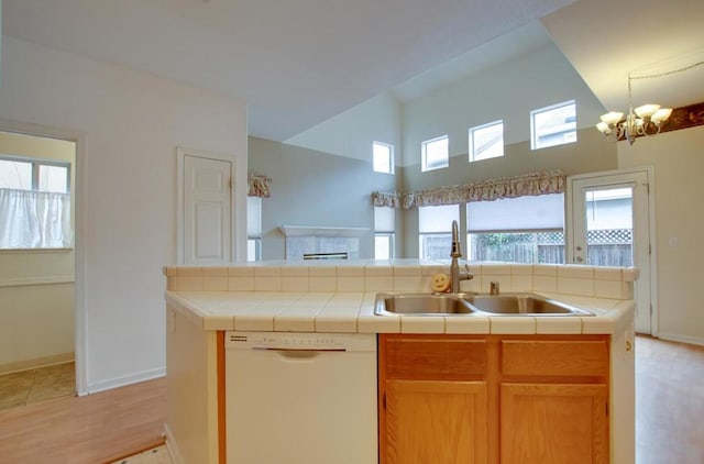 kitchen featuring sink, light wood-type flooring, tile counters, white dishwasher, and a notable chandelier