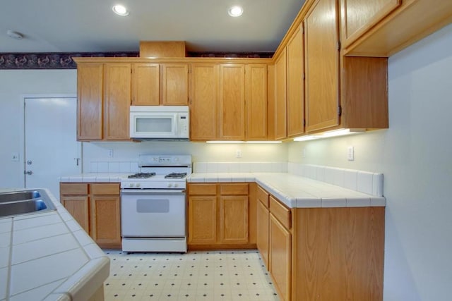 kitchen featuring white appliances, tile counters, and sink