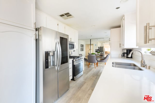 kitchen featuring stainless steel appliances, white cabinetry, sink, and light hardwood / wood-style floors