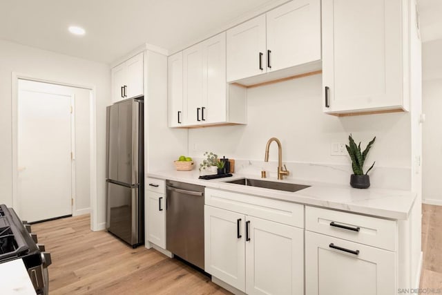 kitchen with appliances with stainless steel finishes, white cabinetry, sink, light stone countertops, and light hardwood / wood-style flooring