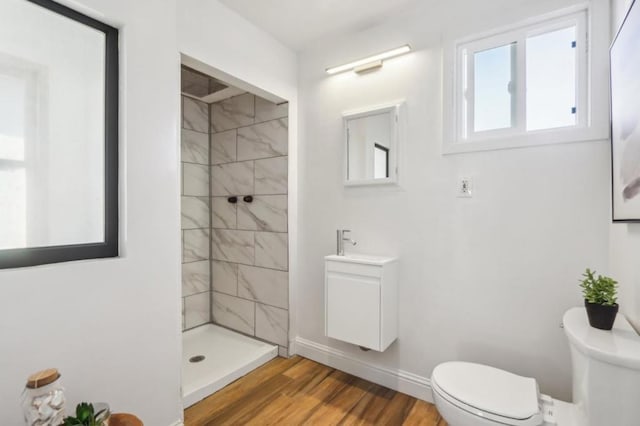 bathroom featuring vanity, tiled shower, hardwood / wood-style floors, and toilet