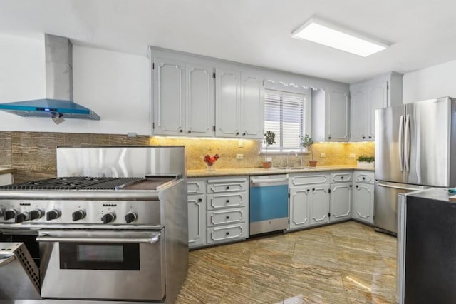 kitchen featuring gray cabinetry, appliances with stainless steel finishes, decorative backsplash, and wall chimney range hood