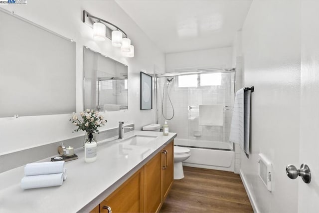 full bathroom featuring hardwood / wood-style flooring, vanity, combined bath / shower with glass door, and toilet