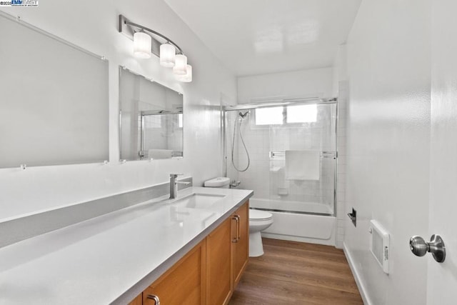 full bathroom featuring hardwood / wood-style flooring, enclosed tub / shower combo, vanity, and toilet