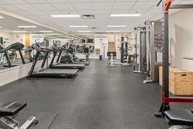 workout area with an AC wall unit and a drop ceiling