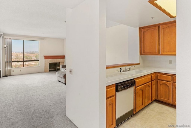 kitchen featuring tasteful backsplash, dishwasher, sink, a tiled fireplace, and light carpet