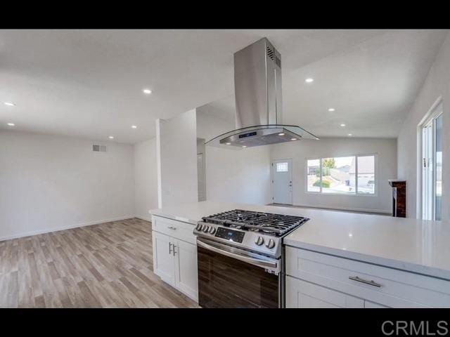 kitchen featuring white cabinetry, island range hood, stainless steel range with gas cooktop, and light hardwood / wood-style flooring