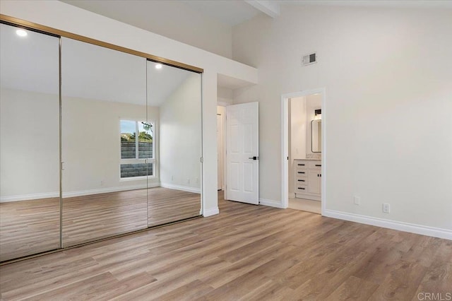 unfurnished bedroom with connected bathroom, high vaulted ceiling, light wood-type flooring, a closet, and beam ceiling