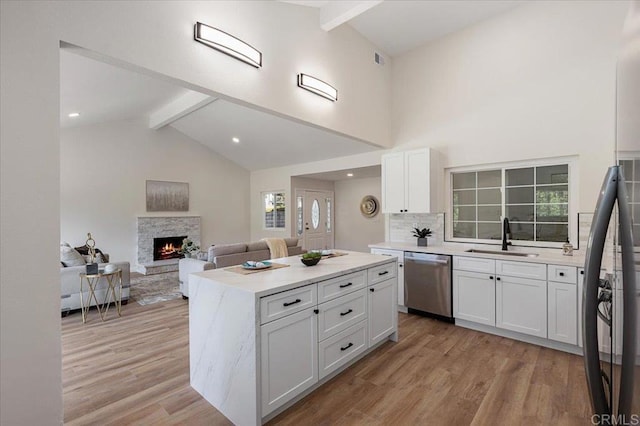 kitchen featuring sink, stainless steel dishwasher, a kitchen island, beamed ceiling, and white cabinets