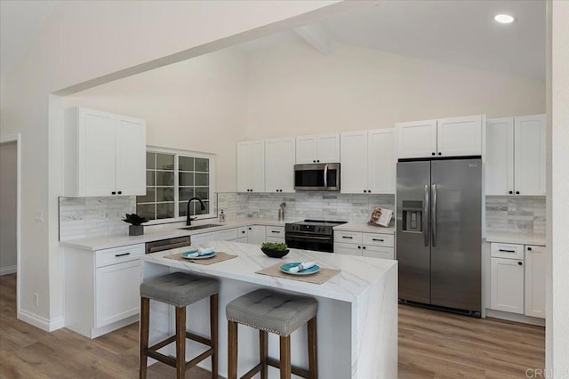 kitchen featuring sink, appliances with stainless steel finishes, a kitchen island, white cabinets, and a kitchen bar