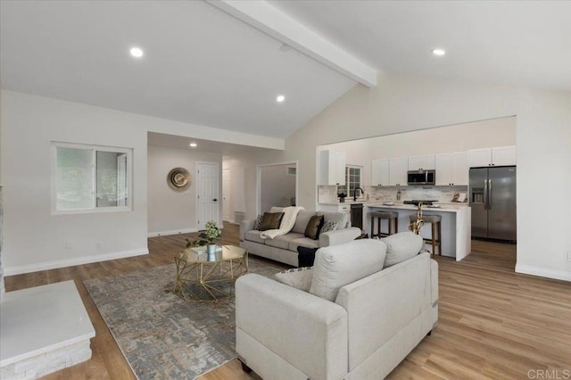 living room featuring sink, high vaulted ceiling, light hardwood / wood-style floors, and beamed ceiling