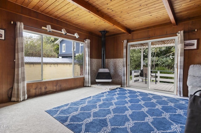 unfurnished sunroom with wood ceiling, beam ceiling, a healthy amount of sunlight, and a wood stove