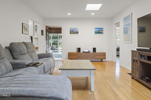 living room featuring light hardwood / wood-style flooring, built in shelves, and a skylight