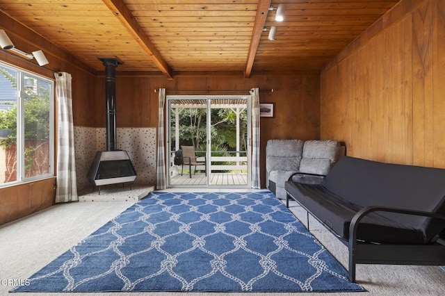 unfurnished room featuring a wood stove, carpet flooring, wooden ceiling, beamed ceiling, and wood walls