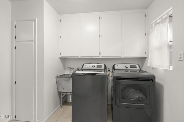 clothes washing area with sink, light tile patterned floors, washer and clothes dryer, and cabinets