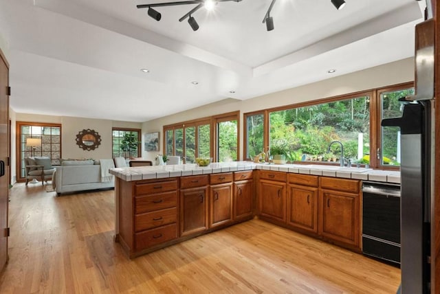 kitchen featuring tile countertops, dishwasher, sink, kitchen peninsula, and light hardwood / wood-style flooring