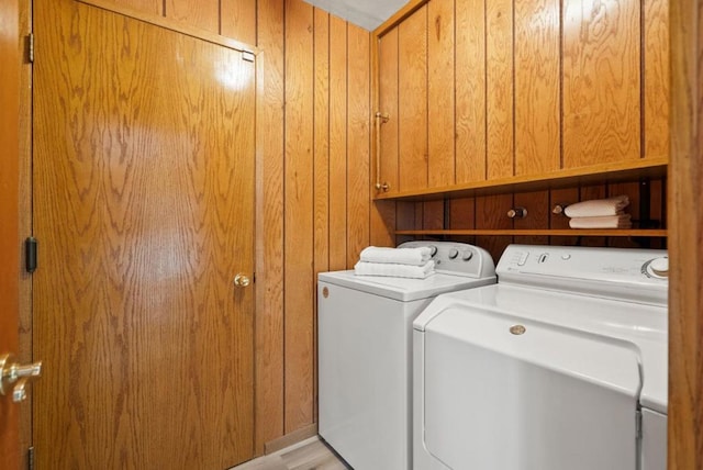 washroom with cabinets, wooden walls, and washer and clothes dryer