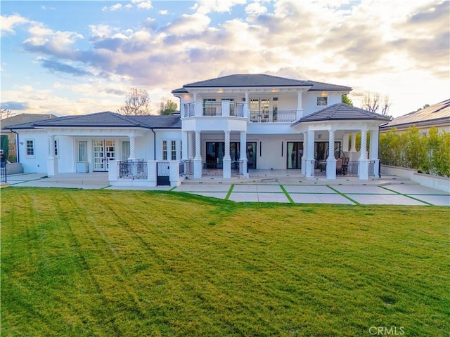 rear view of house with a yard, a patio area, french doors, and a balcony