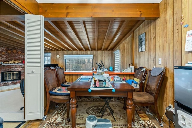 dining room featuring beamed ceiling, wooden walls, and a fireplace