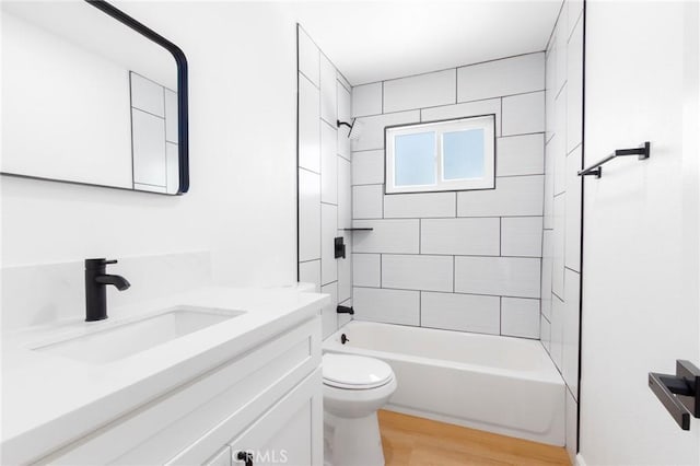 full bathroom with hardwood / wood-style flooring, tiled shower / bath, vanity, and toilet