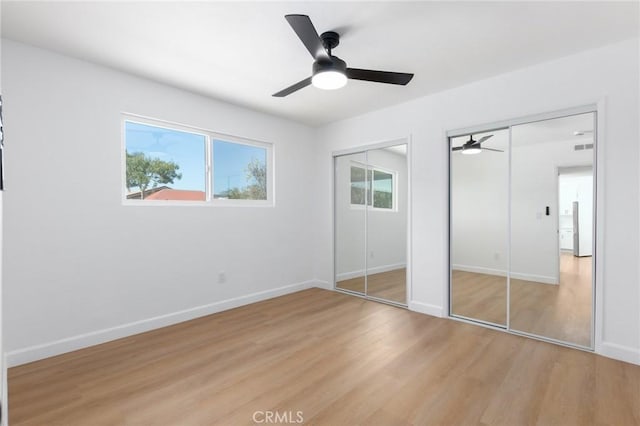 unfurnished bedroom featuring ceiling fan, light hardwood / wood-style flooring, and multiple closets