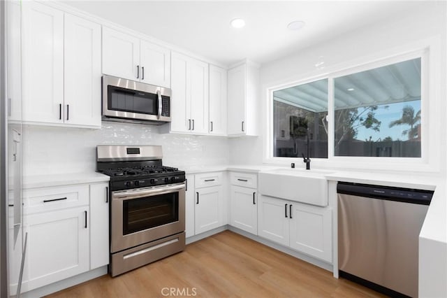 kitchen with appliances with stainless steel finishes, sink, white cabinets, decorative backsplash, and light hardwood / wood-style flooring