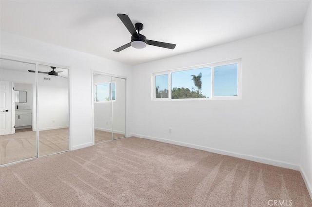 unfurnished bedroom featuring ceiling fan, light colored carpet, and two closets