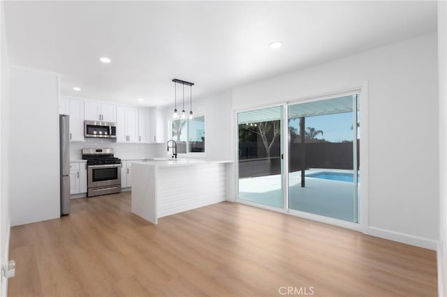 kitchen with appliances with stainless steel finishes, a wealth of natural light, pendant lighting, white cabinetry, and kitchen peninsula