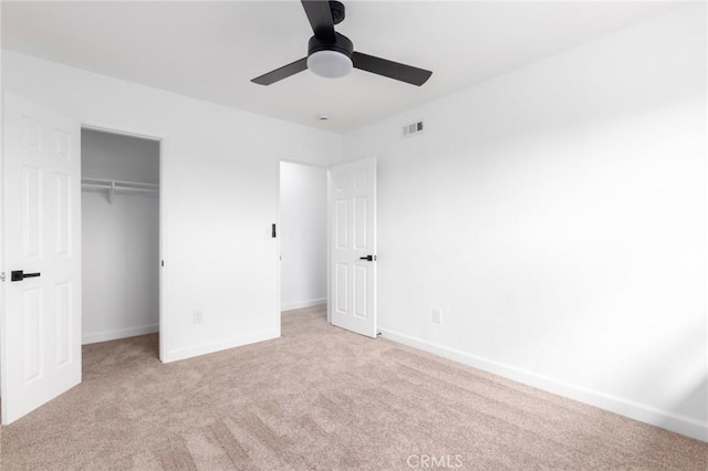 unfurnished bedroom with a walk in closet, light carpet, ceiling fan, and a closet