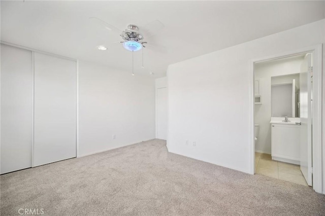 unfurnished bedroom with ensuite bathroom, light carpet, ceiling fan, and a closet