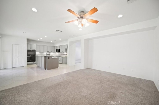 unfurnished living room featuring sink, light colored carpet, and ceiling fan