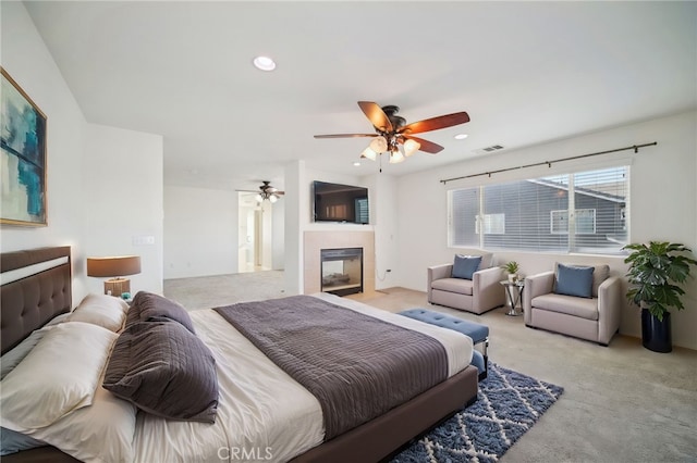 bedroom with ceiling fan, a tiled fireplace, and light carpet