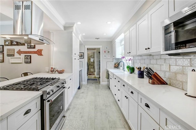 kitchen with appliances with stainless steel finishes, island range hood, white cabinetry, light stone counters, and crown molding