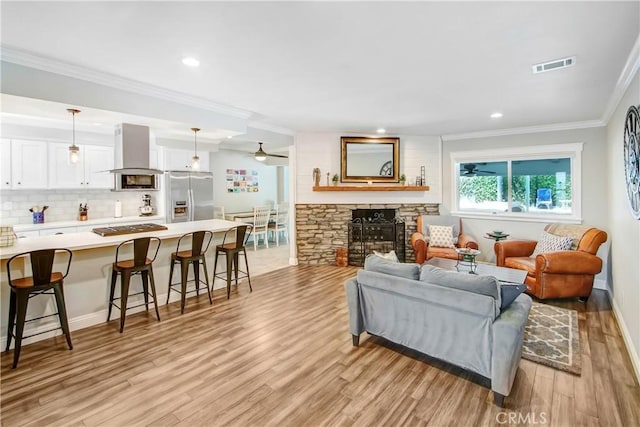 living room featuring crown molding, a stone fireplace, ceiling fan, and light wood-type flooring