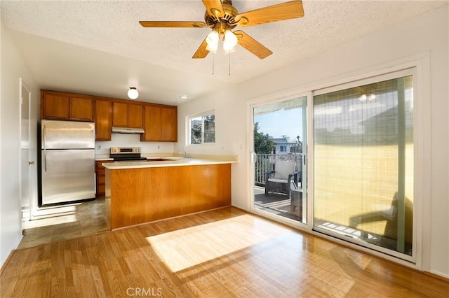 kitchen with stainless steel appliances, kitchen peninsula, a textured ceiling, and light wood-type flooring