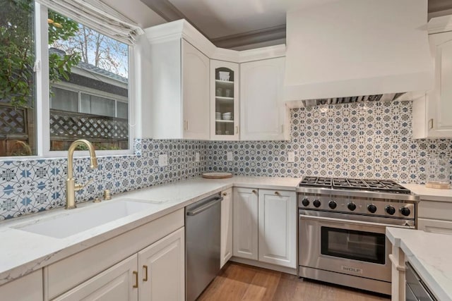 kitchen with sink, white cabinetry, stainless steel appliances, light stone countertops, and light wood-type flooring