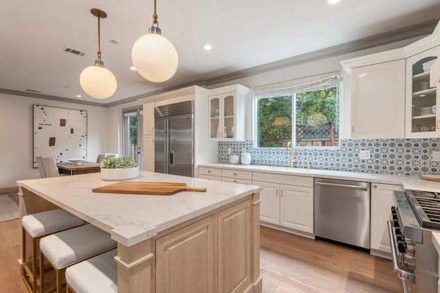 kitchen featuring decorative light fixtures, sink, premium appliances, a center island, and light stone counters