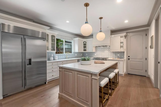 kitchen featuring light stone counters, white cabinetry, built in refrigerator, hanging light fixtures, and a kitchen island