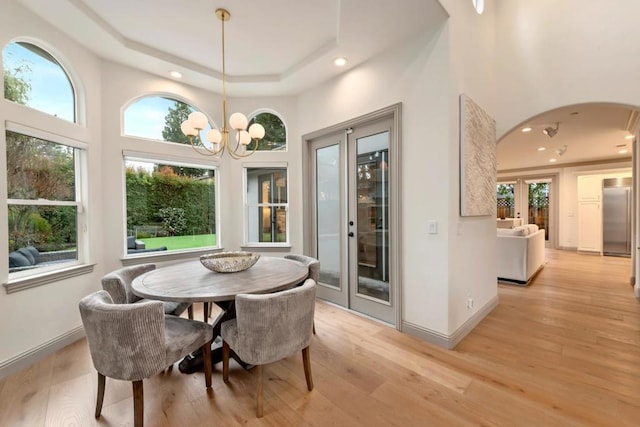 dining room featuring light wood-type flooring, a high ceiling, a tray ceiling, an inviting chandelier, and french doors