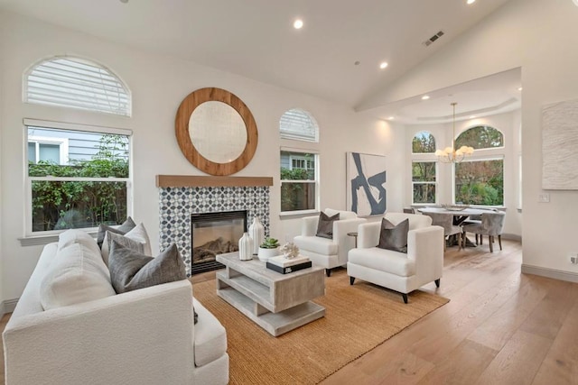 living room with a tile fireplace, a healthy amount of sunlight, high vaulted ceiling, and light hardwood / wood-style flooring