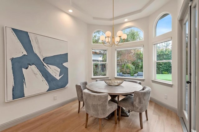 dining room with a notable chandelier, a raised ceiling, and light wood-type flooring