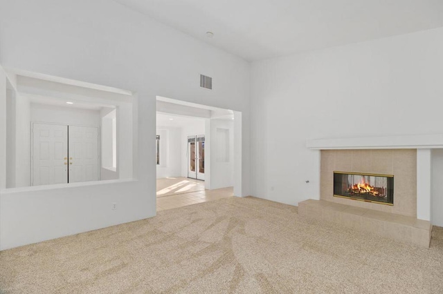 unfurnished living room featuring a tiled fireplace, a high ceiling, and light colored carpet