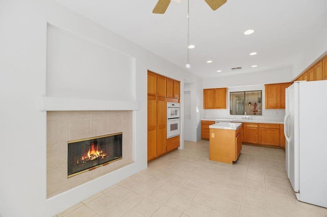 kitchen with sink, white appliances, a tile fireplace, ceiling fan, and a kitchen island