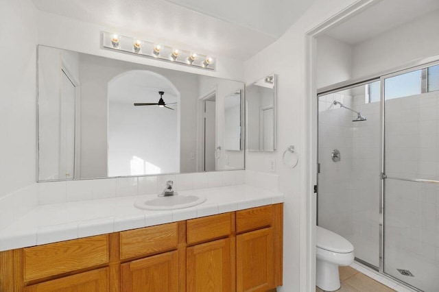 bathroom with ceiling fan, tile patterned flooring, vanity, a shower with shower door, and toilet